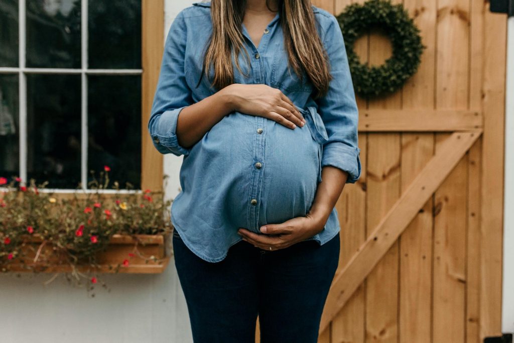Pregnant woman holding her belly in front of a front door and window.