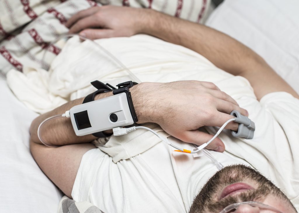 Man getting sleep study with device and cords.